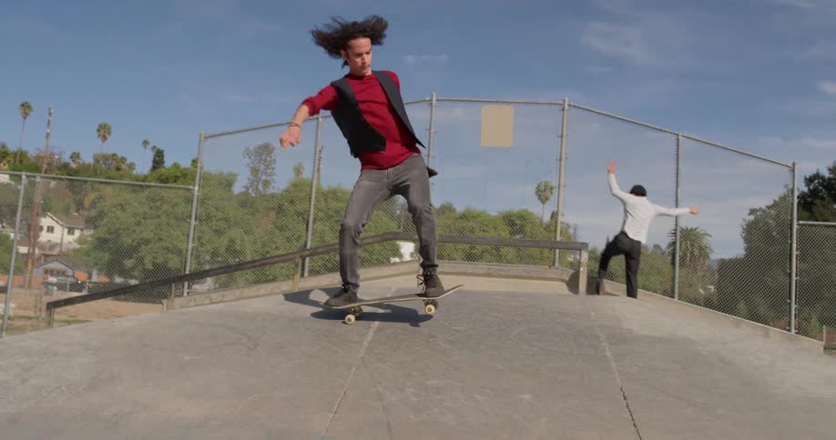 Two men skateboard at a skateboard park on a sunny day