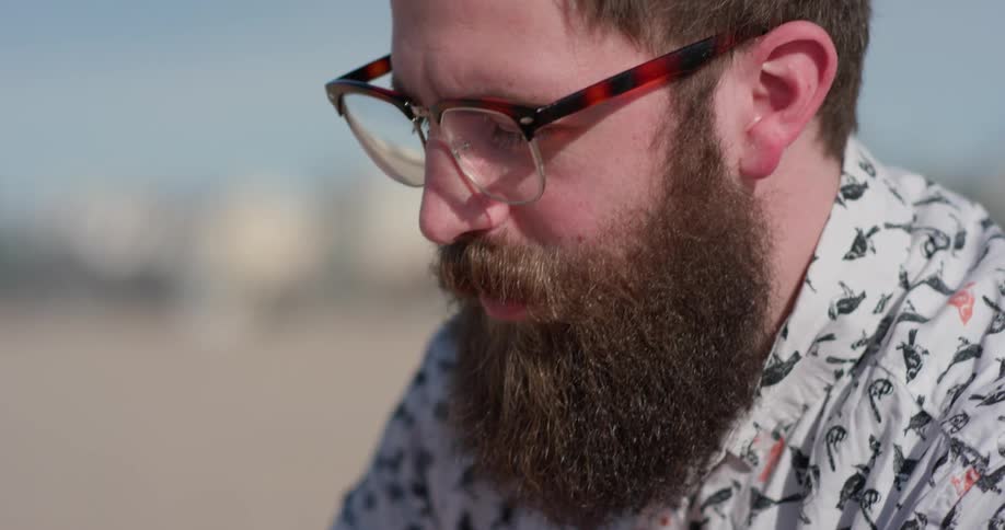 A mean with a thick beard sits outside