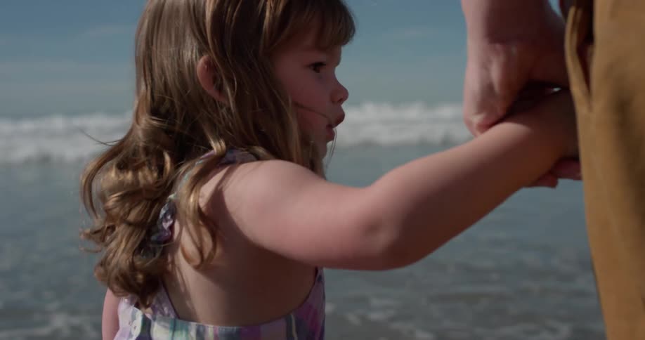 A man holds the hand of a young girl as the tide rolls in