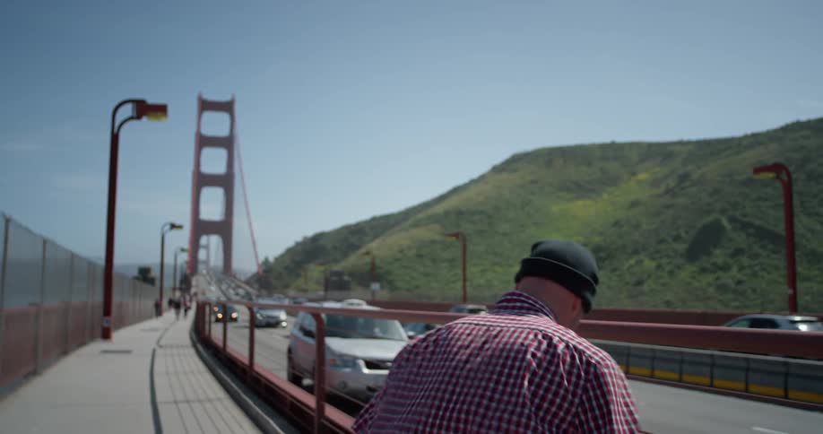 A man skateboards on a bridge's pedestrian path