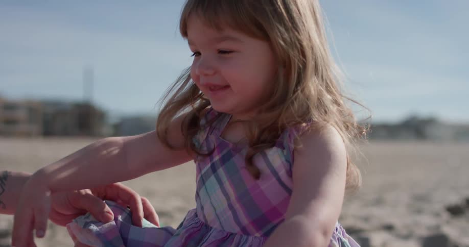 Smiling toddler plays with a yellow truck on the beach