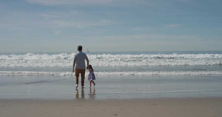 A man and young girl stand on the beach as the tide flows in
