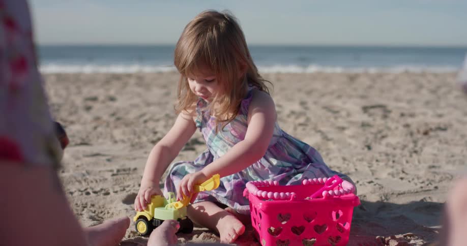 A young girl plays on the beach with plastic toys