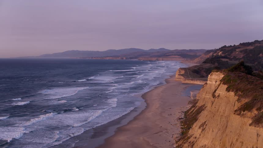 Ocean waves flow towards a shoreline at sunset