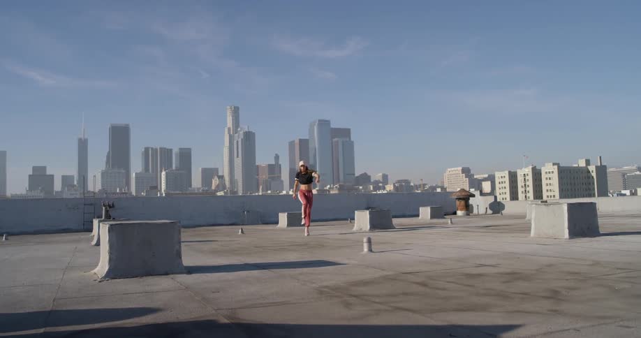 Woman dances on the rooftop in a city on a sunny day