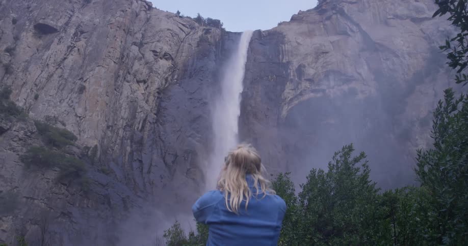 A woman takes a photograph of water falling off the side of the cliff