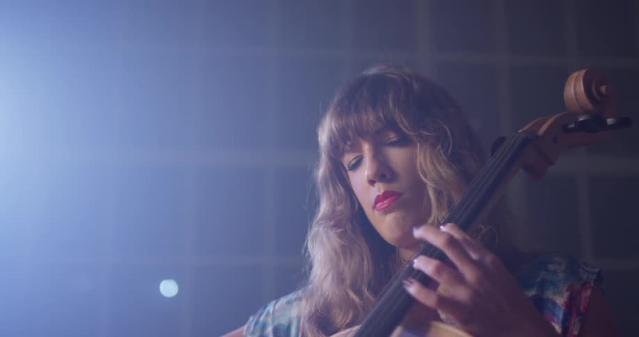 A woman plays a cello in front of a window
