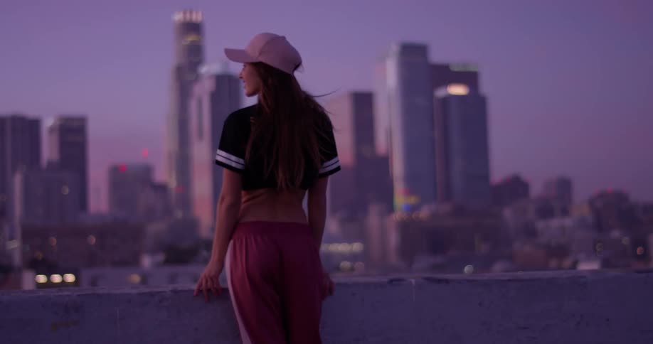 A woman is standing on a rooftop at dawn taking in an urban view