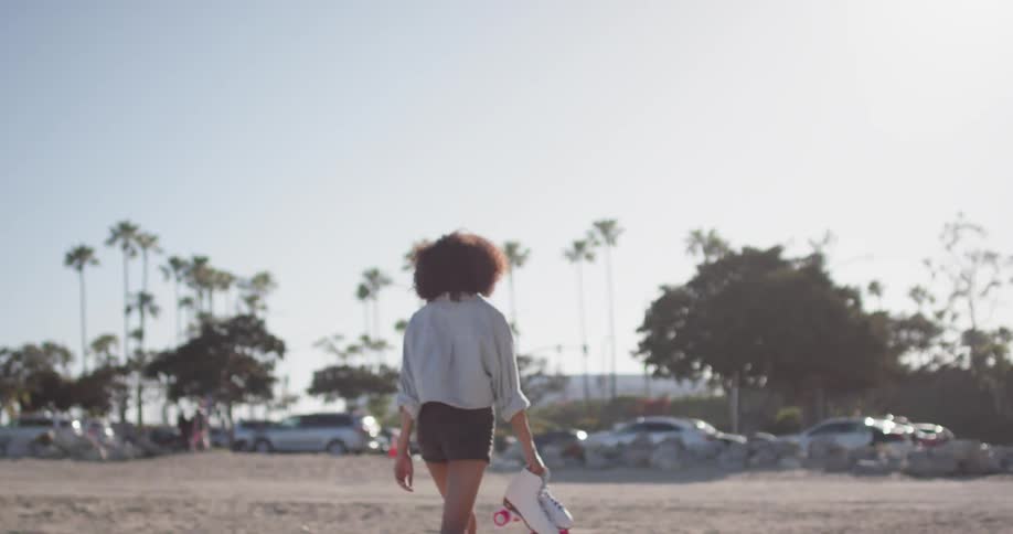 Woman carries roller skates on a large area of sandy ground