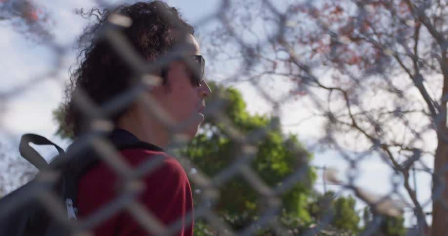 Man with backpack walking past chain link fence