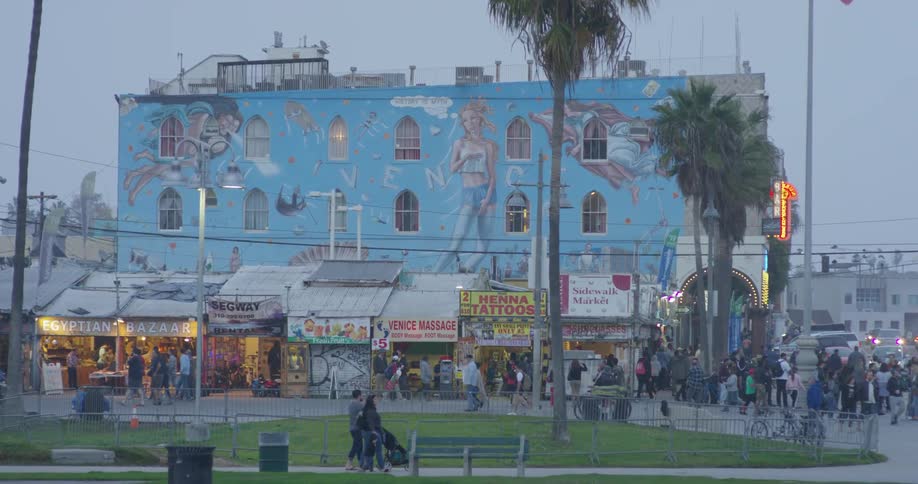 The people are all walking past the large blue building