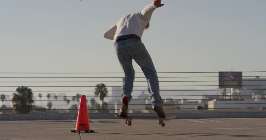 Man jumps skateboard over traffic cone on urban roof