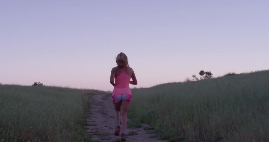 A woman jogs in a rural field at sunset