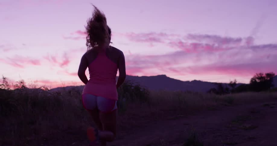 A woman jogs on a ridge trail at sunset