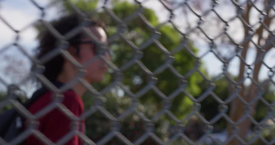 A person walks past the fence wearing sunglasses