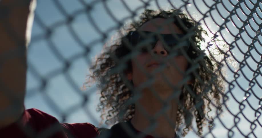A man stands next to a chain link fence on a sunny day