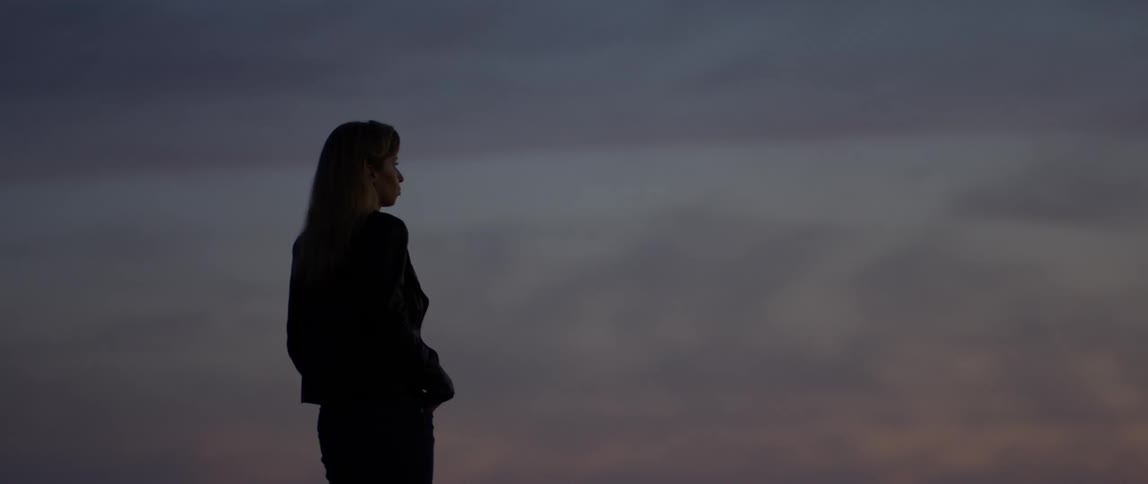 A woman stands outside at dusk