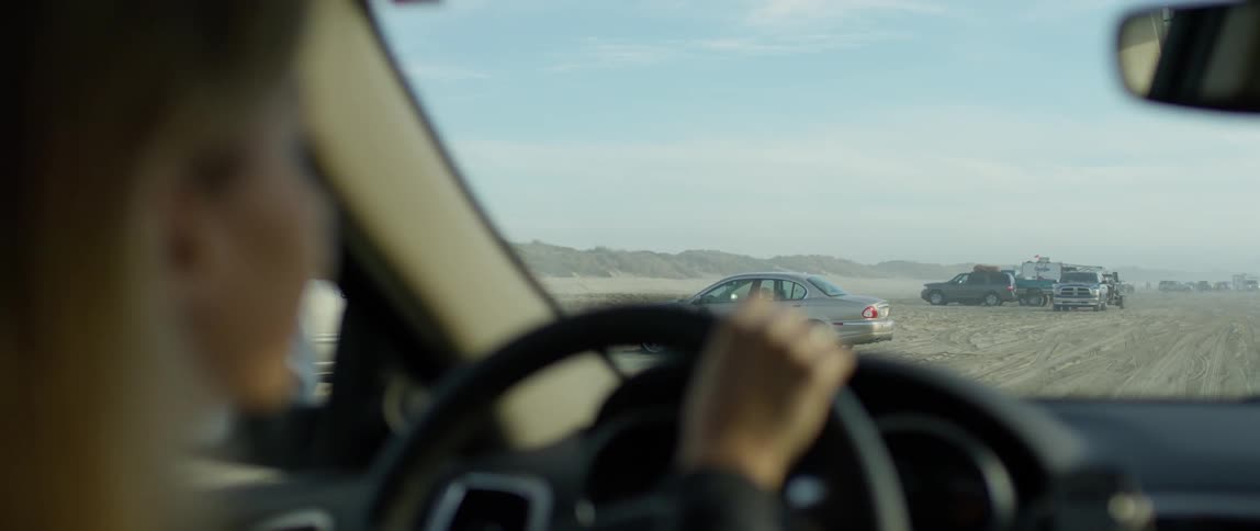 A woman drives a car past cars parked on the sand