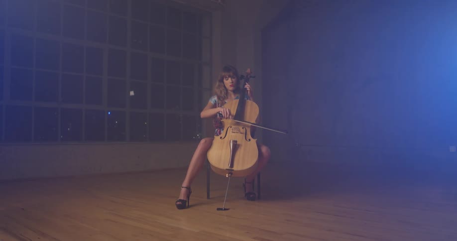 Woman plays the cello in an empty room with a large window at night