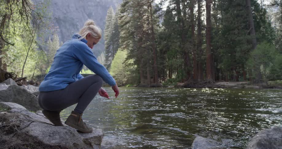 A woman reaches down to touch the stream water