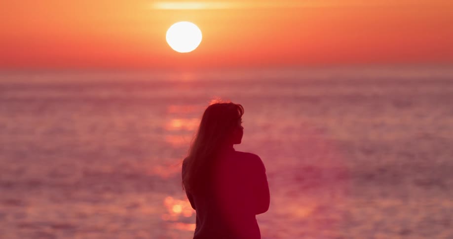 Woman stands on the beach at sunset