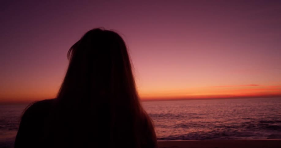 A woman stands on a beach at sunset