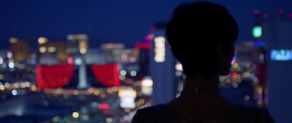Person stands on a tall building looking out at the city at night