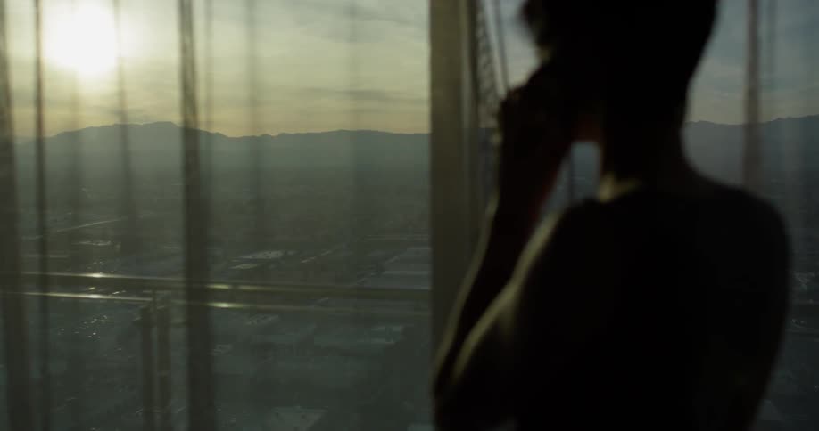 A woman talks on a phone next to a window at sunset