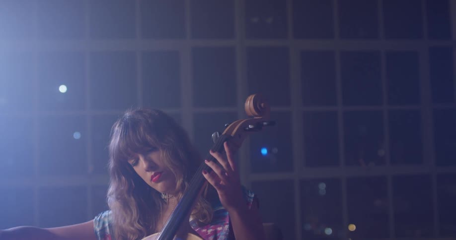 A woman plays a cello in front of windows