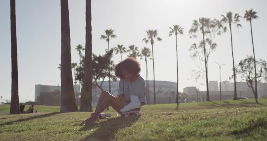 A woman sits on the grass holding roller skates