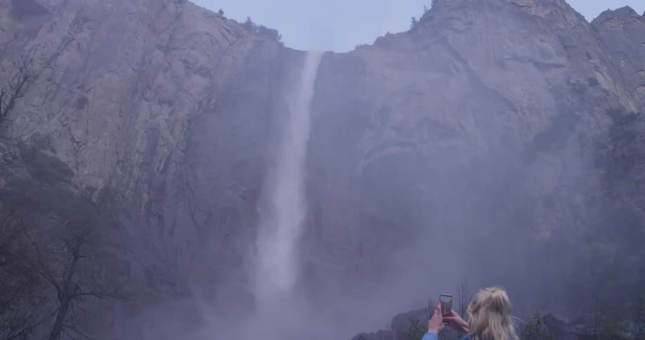 A woman films a waterfall on her phone