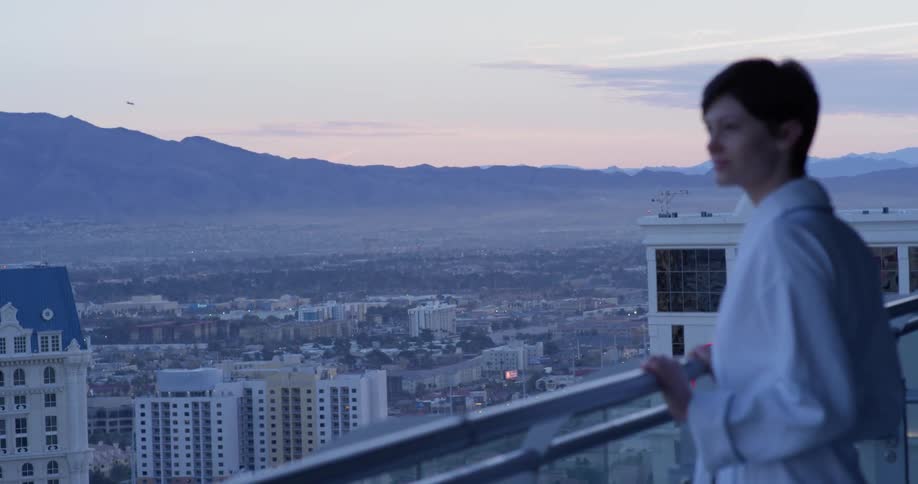 A woman walks on her balcony wearing a white robe