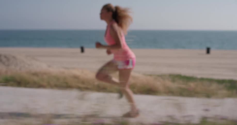 Woman jogs on a sidewalk next to the beach