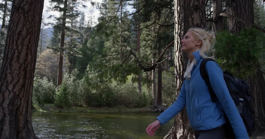 The woman is walking past the lake in the woods
