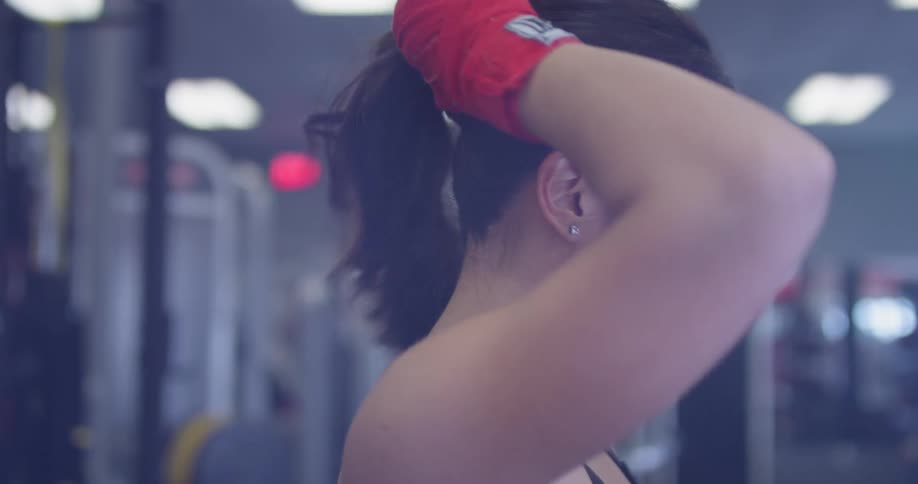 A woman puts her hair into a ponytail in a gym