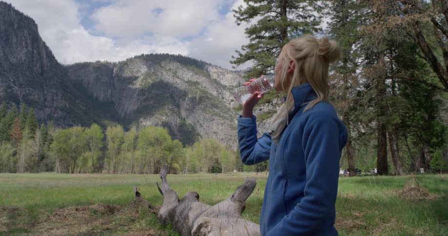 A woman drinks from a water bottle near the mountains