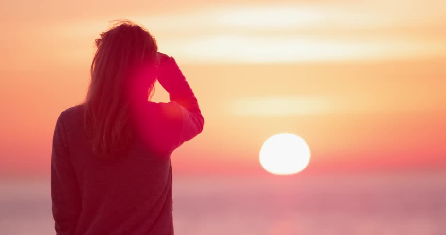 The silhouette of a woman watching an ocean sunset