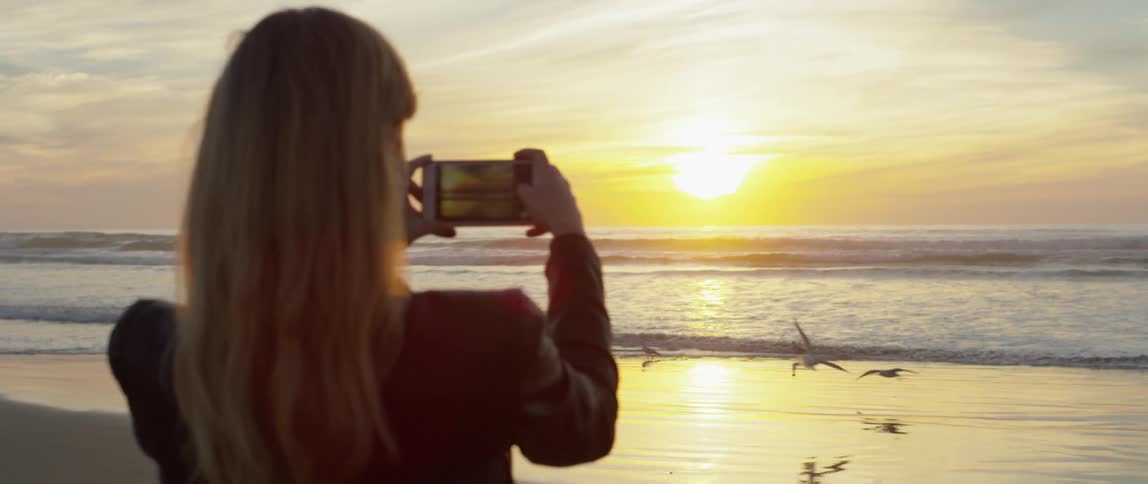 A woman photographs a beach at sunset