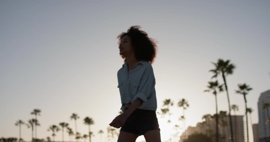 A woman roller skates by the beach at sunset
