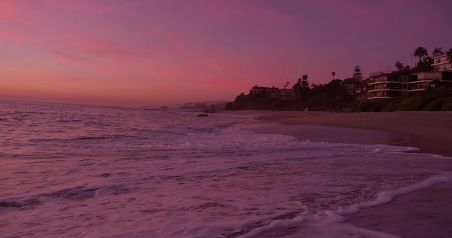 Ocean waves flow to a sandy shore at sunset