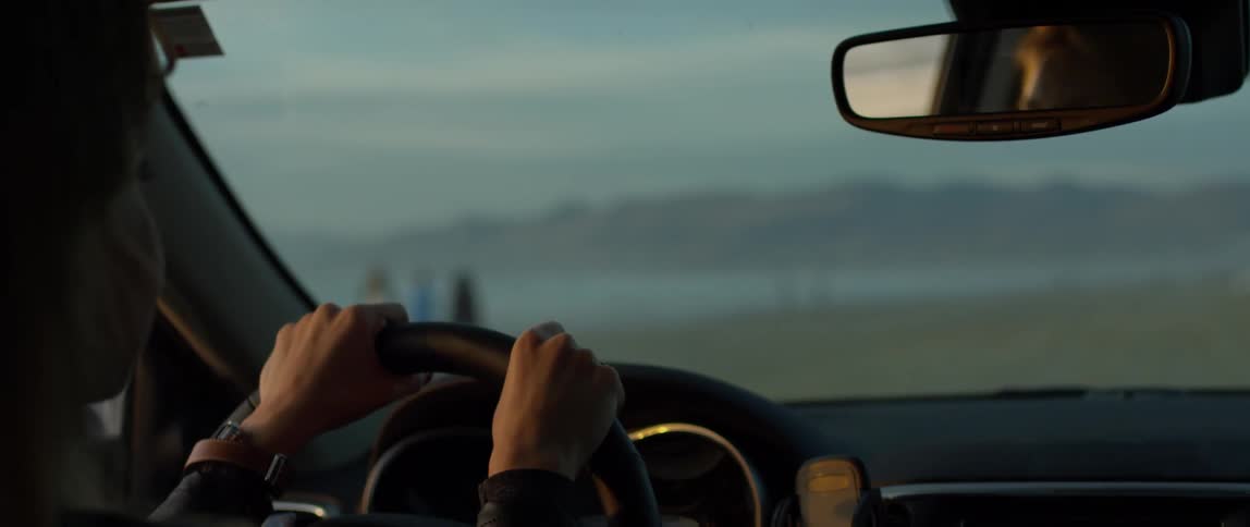 Person driving a car on the beach looks at people standing outside