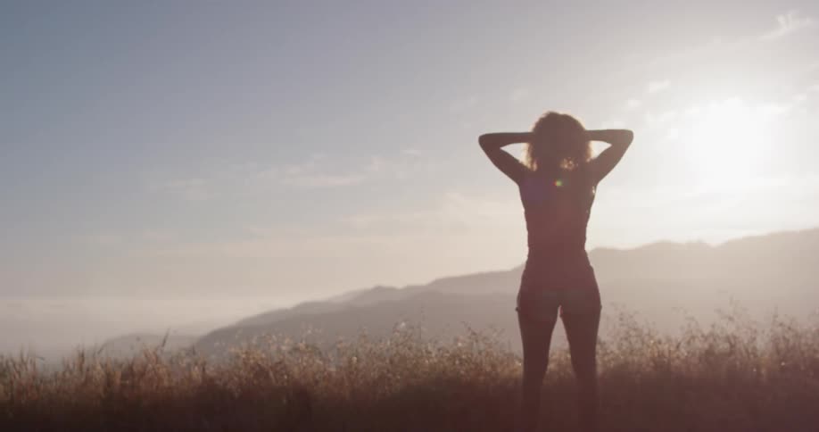 Woman stands outside in nature on a sunny day with her arms raised