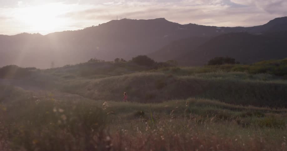 Woman jogs on a path through grassy hills on a sunny day