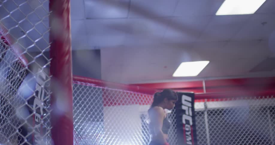 Woman walks into a fenced in area in a gym and practices punching