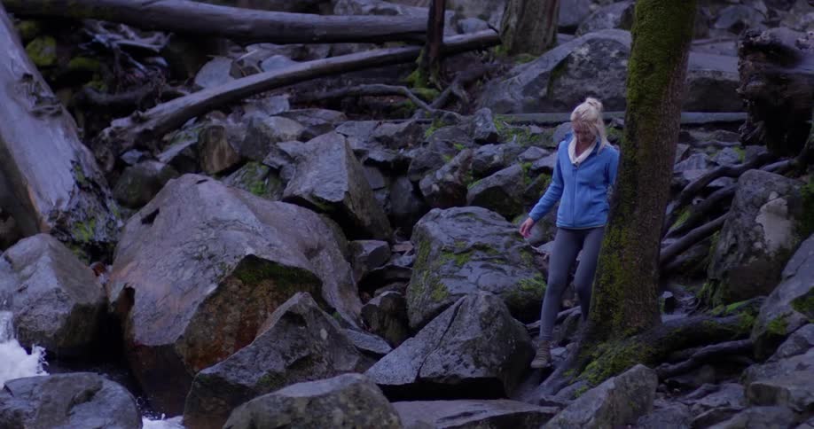 Woman walks on large boulders near a flowing body of water