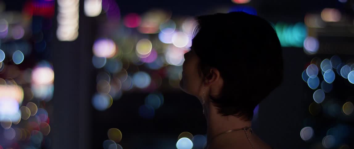 Woman looks out at the lit up city at night