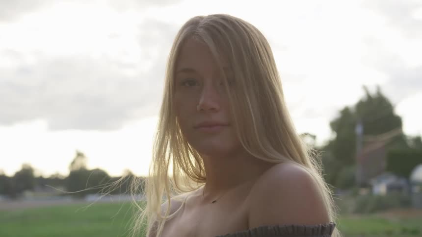 A woman stands in a rural field at sunset