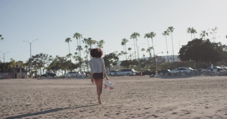 Woman is walking on beach and carrying roller skates