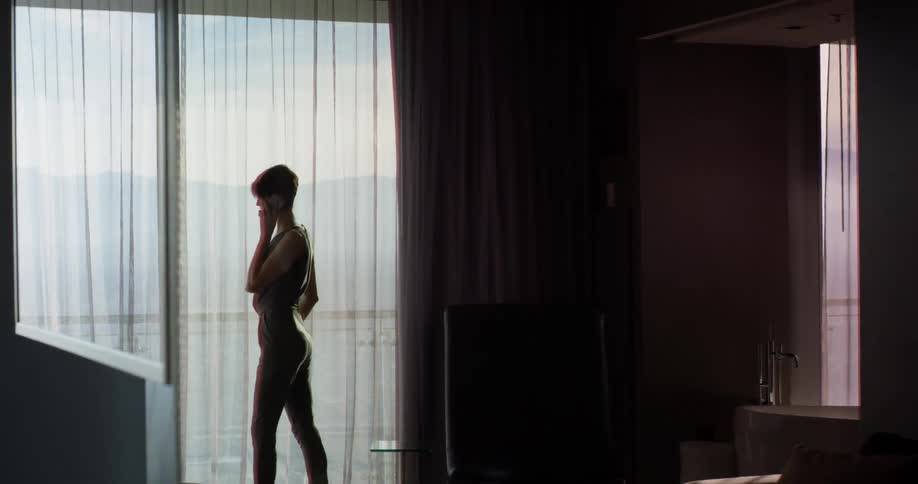 Woman talks on her cell phone as she pushes the curtains back