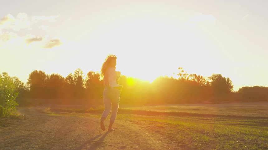 A woman walks on the field at sunset